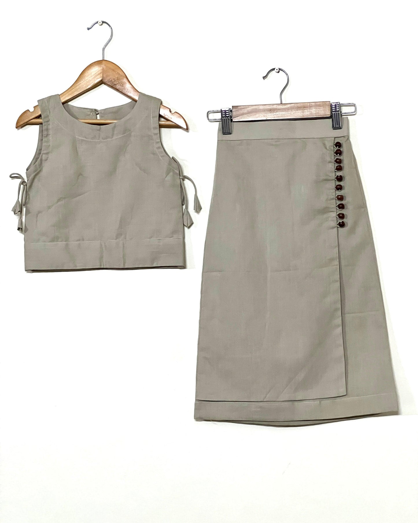 Beige linen co-ord set for young girls featuring a sleeveless top with side ties and a wrap skirt with wooden button details—perfect for stylish comfort.
