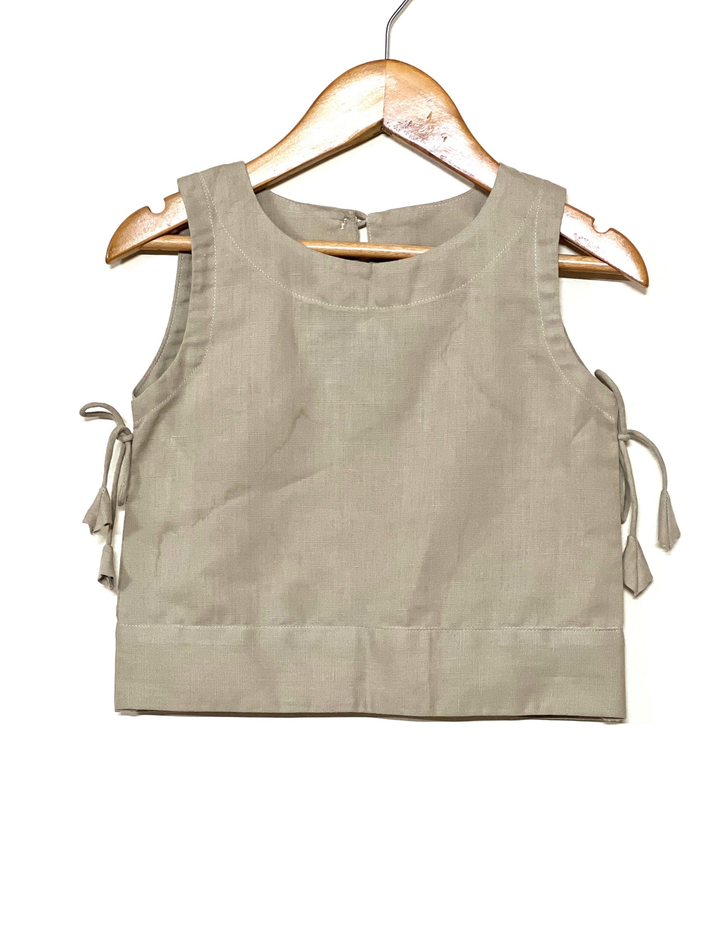 Beige linen co-ord set for young girls featuring a sleeveless top with side ties and a wrap skirt with wooden button details—perfect for stylish comfort.